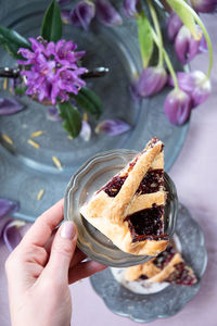 A piece of raspberry layer cake in a woman's hand lilac spring tulips on a plate