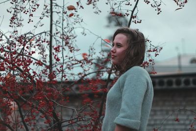 Side view of young woman looking away against trees