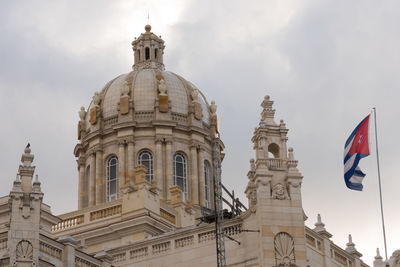 Low angle view of cuban flag by historic building against sky