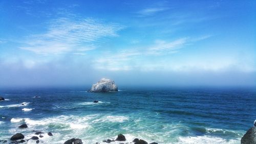 Scenic view of sea and rocks with fog rolling in against sky
