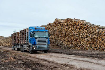 View of truck by logs stack against sky
