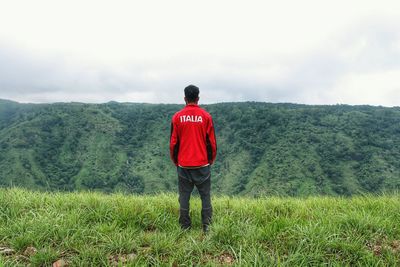 Rear view of man standing on grassy field against mountain