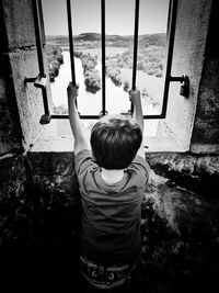 Rear view of boy looking through window