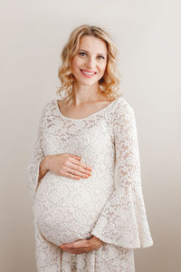 Portrait of smiling pregnant woman touching abdomen against white background