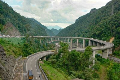 Bridge over road by mountains against sky