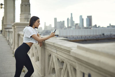 Woman using mobile phone leaning on bridge in city