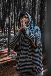 Young man standing against tree trunk in forest