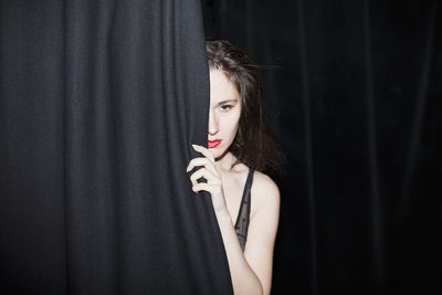 Portrait of a beautiful young woman standing against curtain