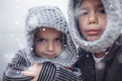 Girl in knitted grey hat hugging her frozen smaller brother