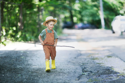 Cute boy with fishing rod walking on road