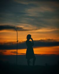 Silhouette woman standing against orange sky during sunset