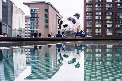 Reflection of people on swimming pool against buildings in city