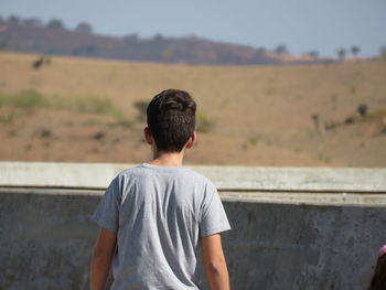 Rear view of boy standing against retaining wall