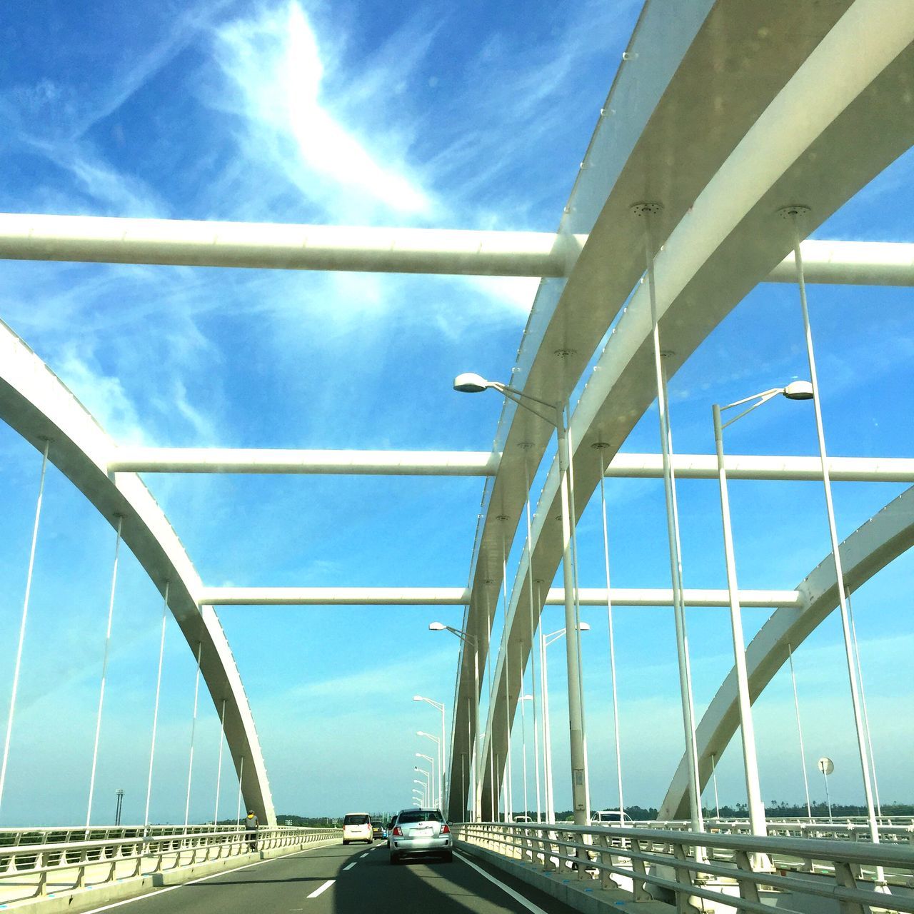 transportation, bridge - man made structure, connection, built structure, architecture, engineering, bridge, the way forward, sky, car, road, blue, low angle view, diminishing perspective, mode of transport, sunlight, land vehicle, suspension bridge, vanishing point, railing