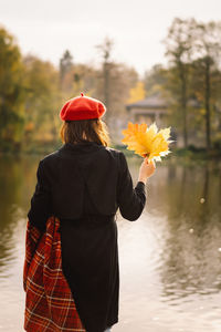 A teengirl in a red beret with a bouquet of autumn leaves in her hands walks on wooden pontoon