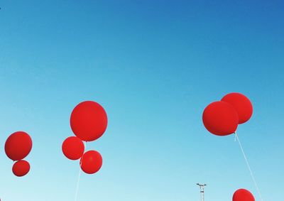 Low angle view of red helium balloons against clear sky