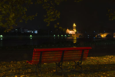 Empty bench by river in park at night