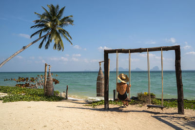 Rear view of woman sitting on swing at beach