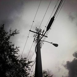 Low angle view of electricity pylon against cloudy sky