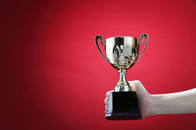 Cropped hand of woman holding trophy against red background