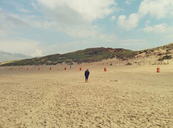 Rear view of man walking at beach against sky