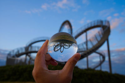 Close-up of hand holding crystal ball against roller coaster