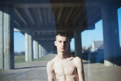 Portrait of young man standing against bridge
