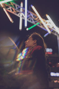 Digital composite image of woman standing against illuminated lights at night