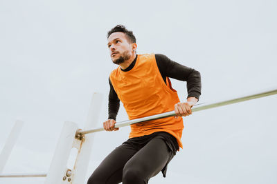 Man exercising on gymnastics bar against sky