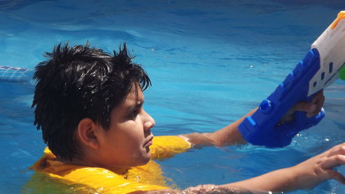 Close-up of boy holding squirt gun while swimming in pool