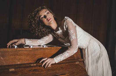 Thoughtful woman in wedding dress leaning on piano at home