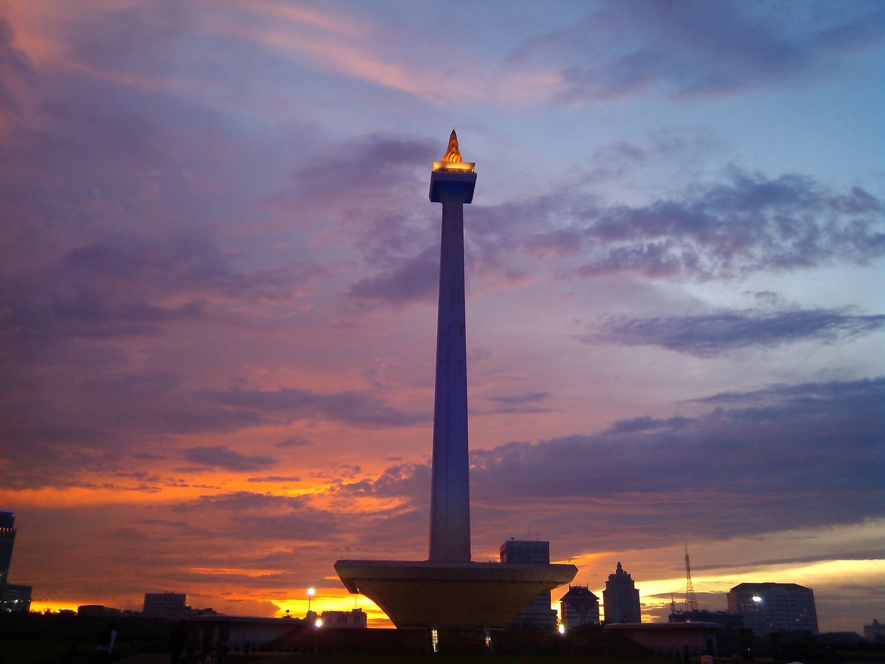 sunset, building exterior, architecture, built structure, sky, cloud - sky, low angle view, orange color, street light, silhouette, tower, city, lighthouse, cloud, lighting equipment, cloudy, tall - high, dusk, guidance, dramatic sky