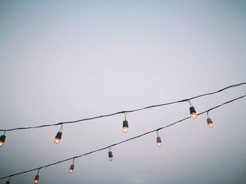 Low angle view of illuminated light bulbs against clear sky