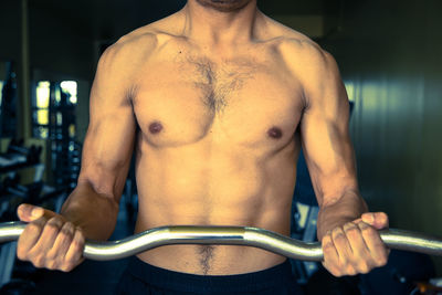 Midsection of shirtless man exercising at gym