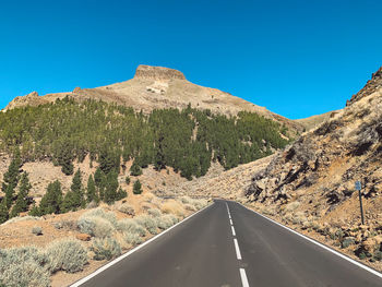 Road leading towards mountain against clear blue sky