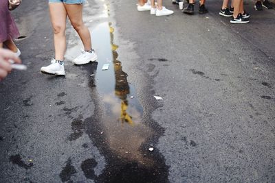 Low section of people standing on road by puddle