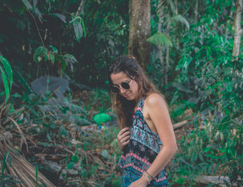 Young woman wearing sunglasses standing by plants in forest