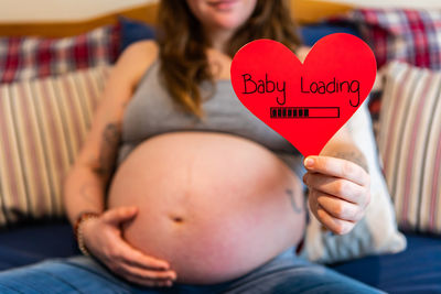 Midsection of pregnant woman holding heart shape at home