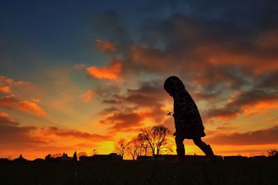 Silhouette of people standing on landscape at sunset