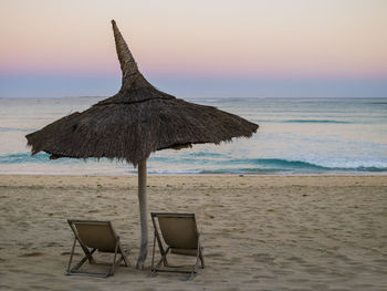 Chair on beach against sky during sunset