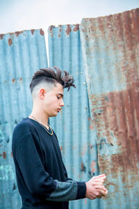 Side view of young man looking away while standing on metal wall