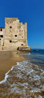 Castle on beach against clear blue sky