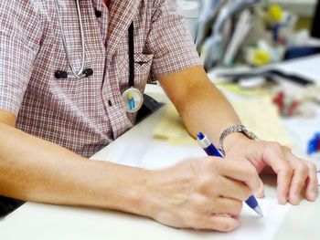 Midsection of doctor writing medical prescription in clinic