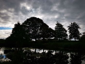 Silhouette trees by lake against sky