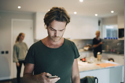 Mature man using mobile phone with family standing in background