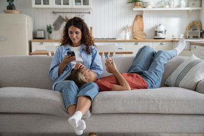 Caucasian mother and daughter relaxing on sofa in living room use mobile phones with social networks