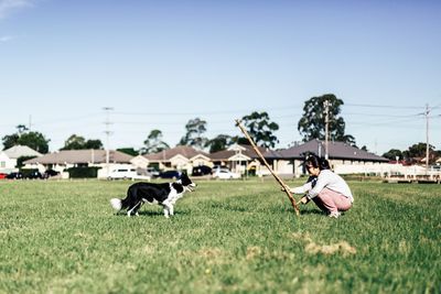 Woman playing with dog on field against clear sky