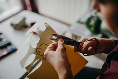 Midsection of man cutting paper with scissors at home