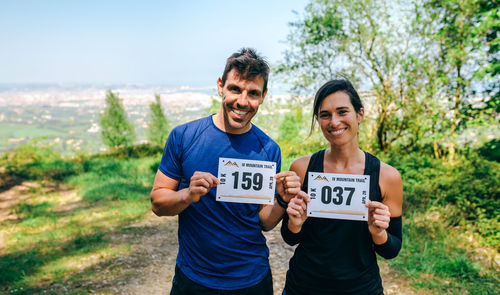 Portrait of smiling athletes holding label on mountain