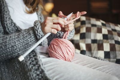 Midsection of woman knitting wool at home
